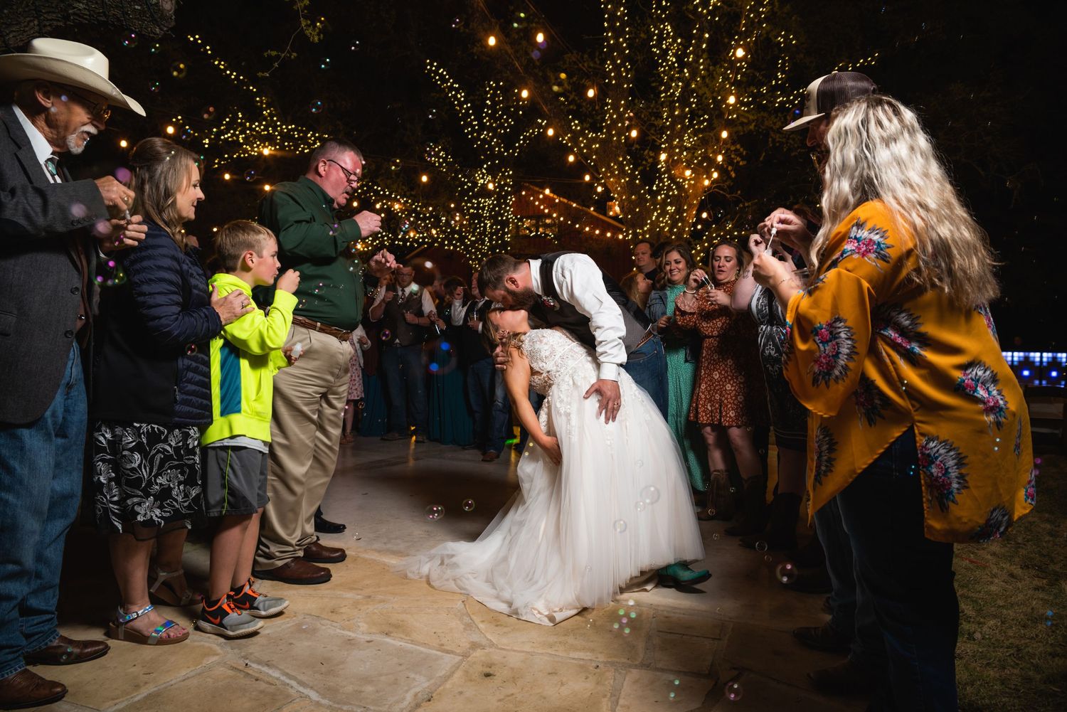 Wedding guests line up for the bride's grand exit under string-lit trees.