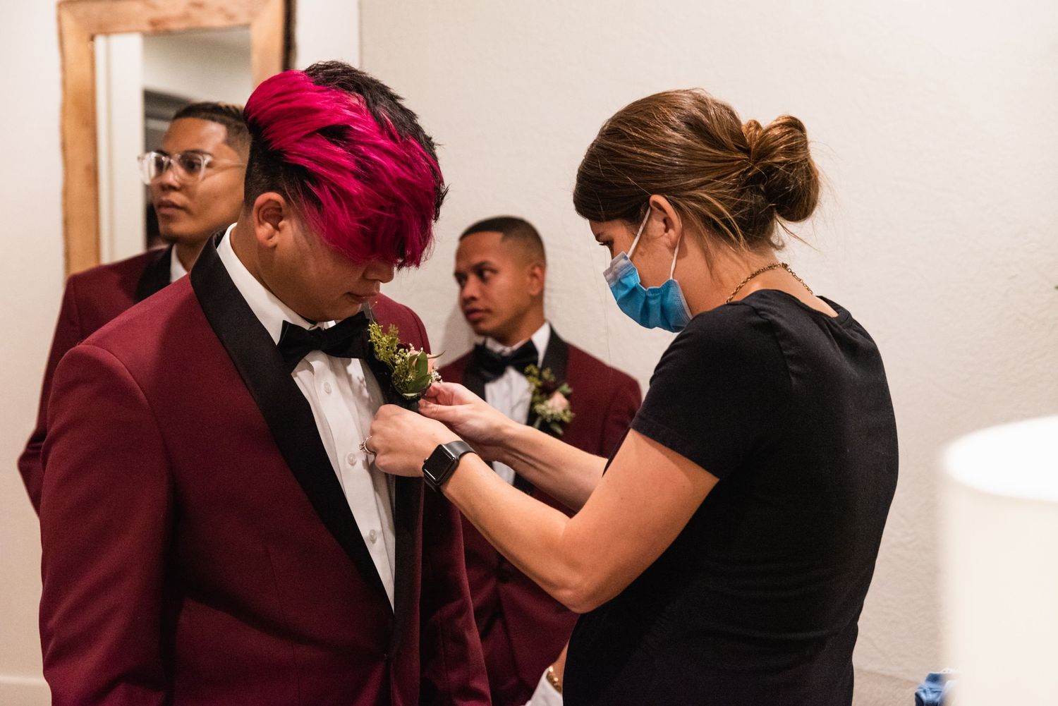 A wedding attendant pins a boutonniere on a burgundy tuxedo jacket.
