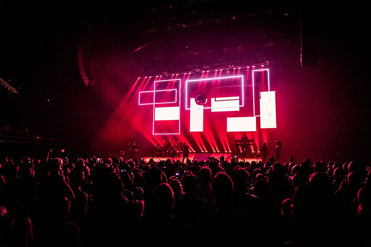 Large neon sign illuminates concert venue with silhouetted crowd in foreground.