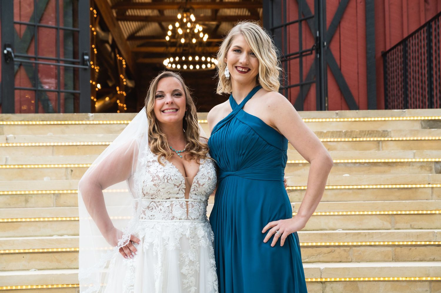 Wedding photo of bride in white dress with bridesmaid in blue on rustic barn steps.