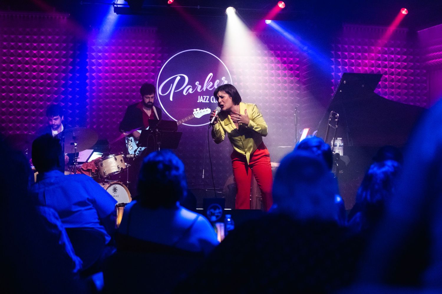 Musicians perform live at Parker Jazz Club with dramatic blue and pink stage lighting.