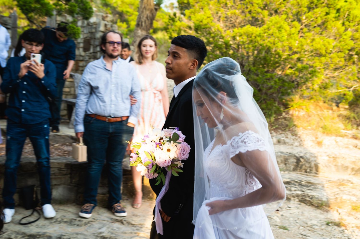 Outdoor wedding ceremony with guests watching couple exchange vows against natural backdrop.
