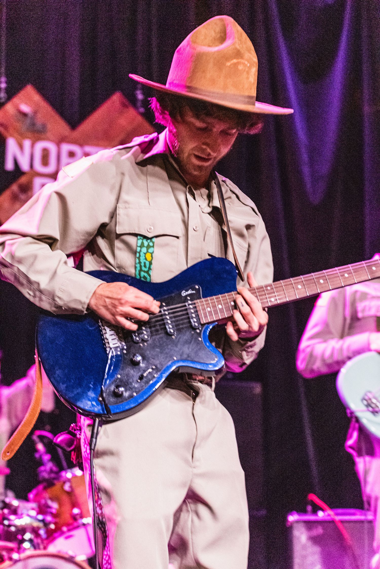Musician wearing brown cowboy hat performs on blue electric guitar during concert performance.