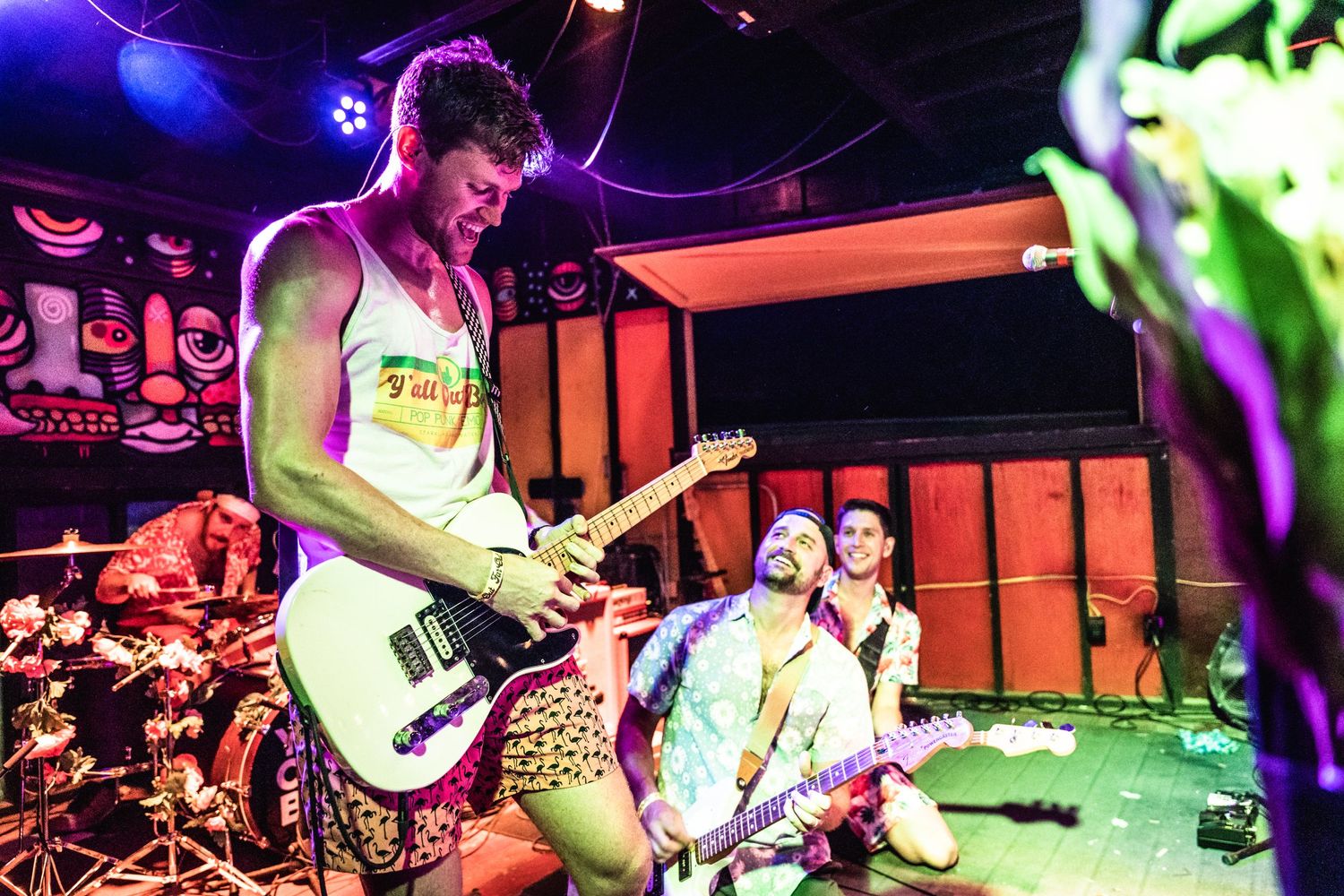 A musician performs energetically on stage with a guitar under colorful lighting.