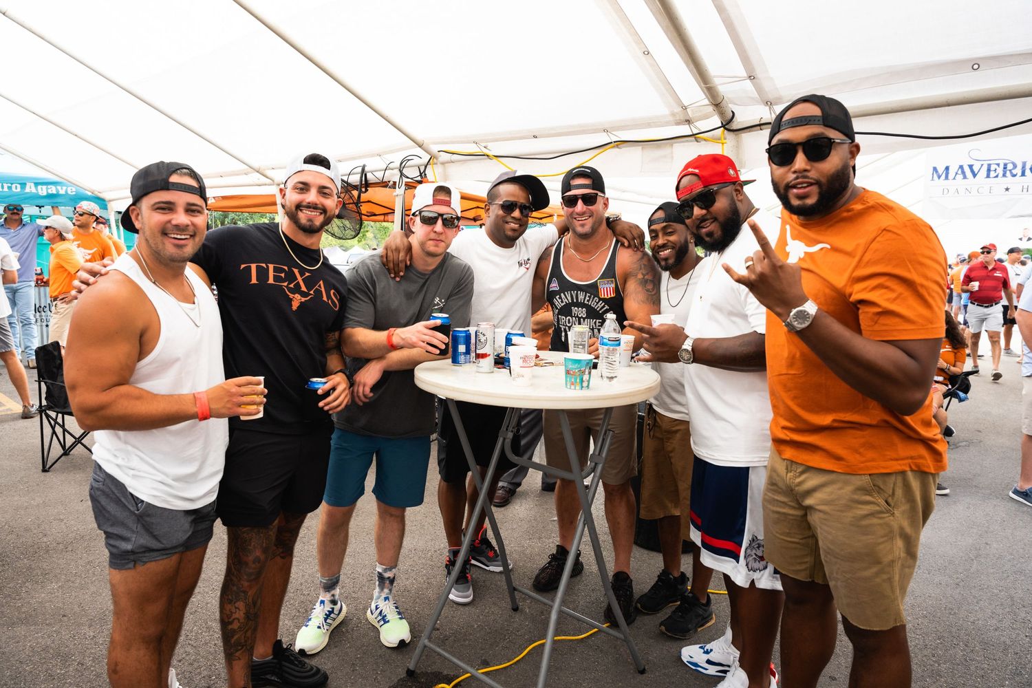 Group of friends enjoying drinks and socializing at an outdoor event under a white tent.
