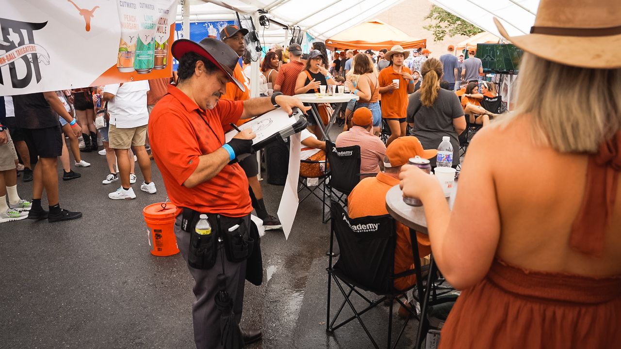 People in orange shirts engage with attendees at outdoor festival booth.