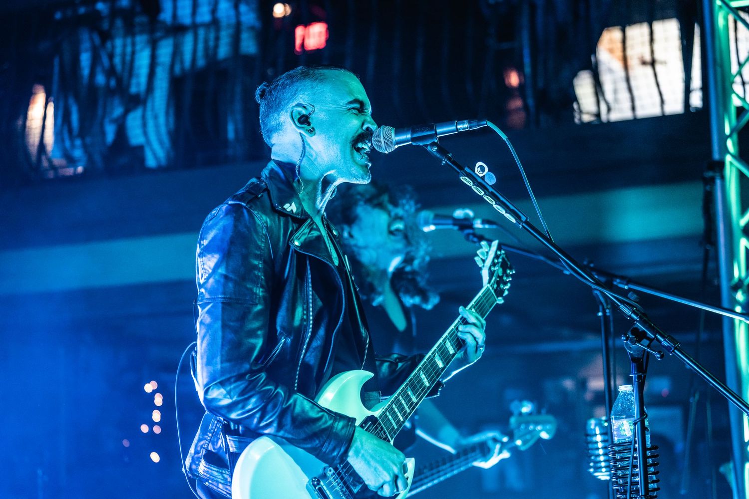 Musician playing guitar and singing into microphone with blue stage illumination.