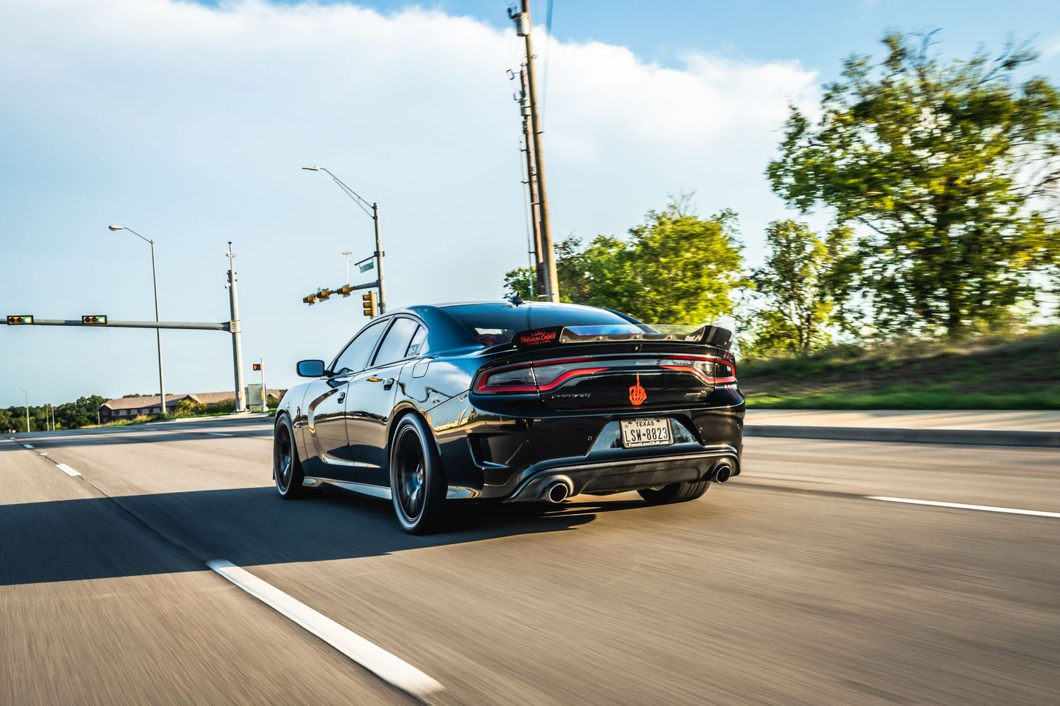 Modified black Dodge Charger with sport wheels photographed in motion on city street.