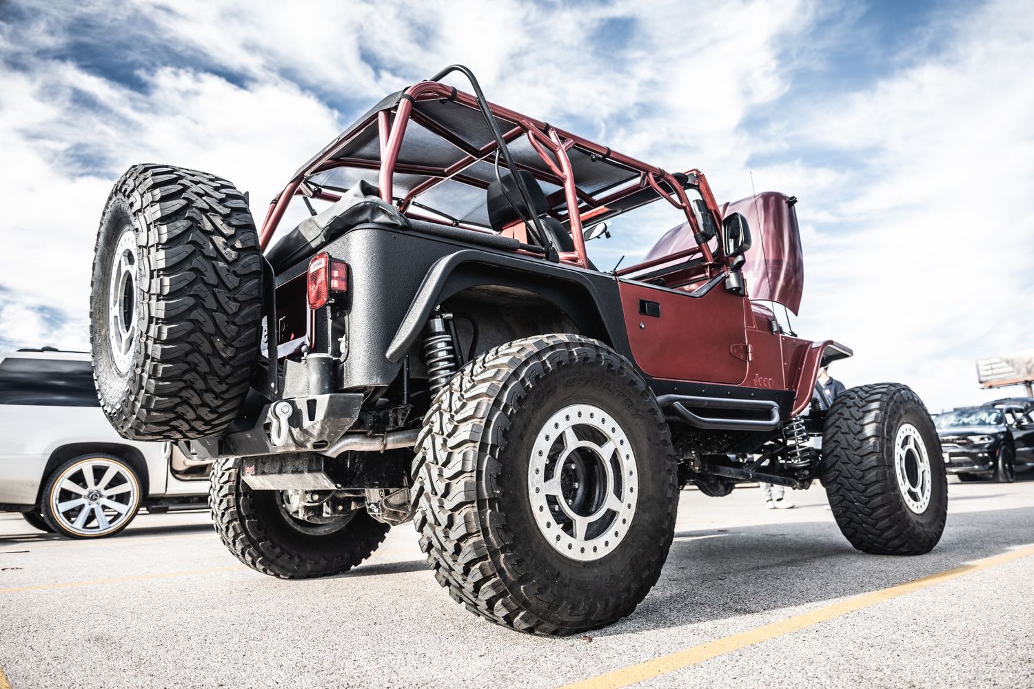 A customized red Jeep Wrangler with large off-road tires and lifted suspension parked under cloudy skies.