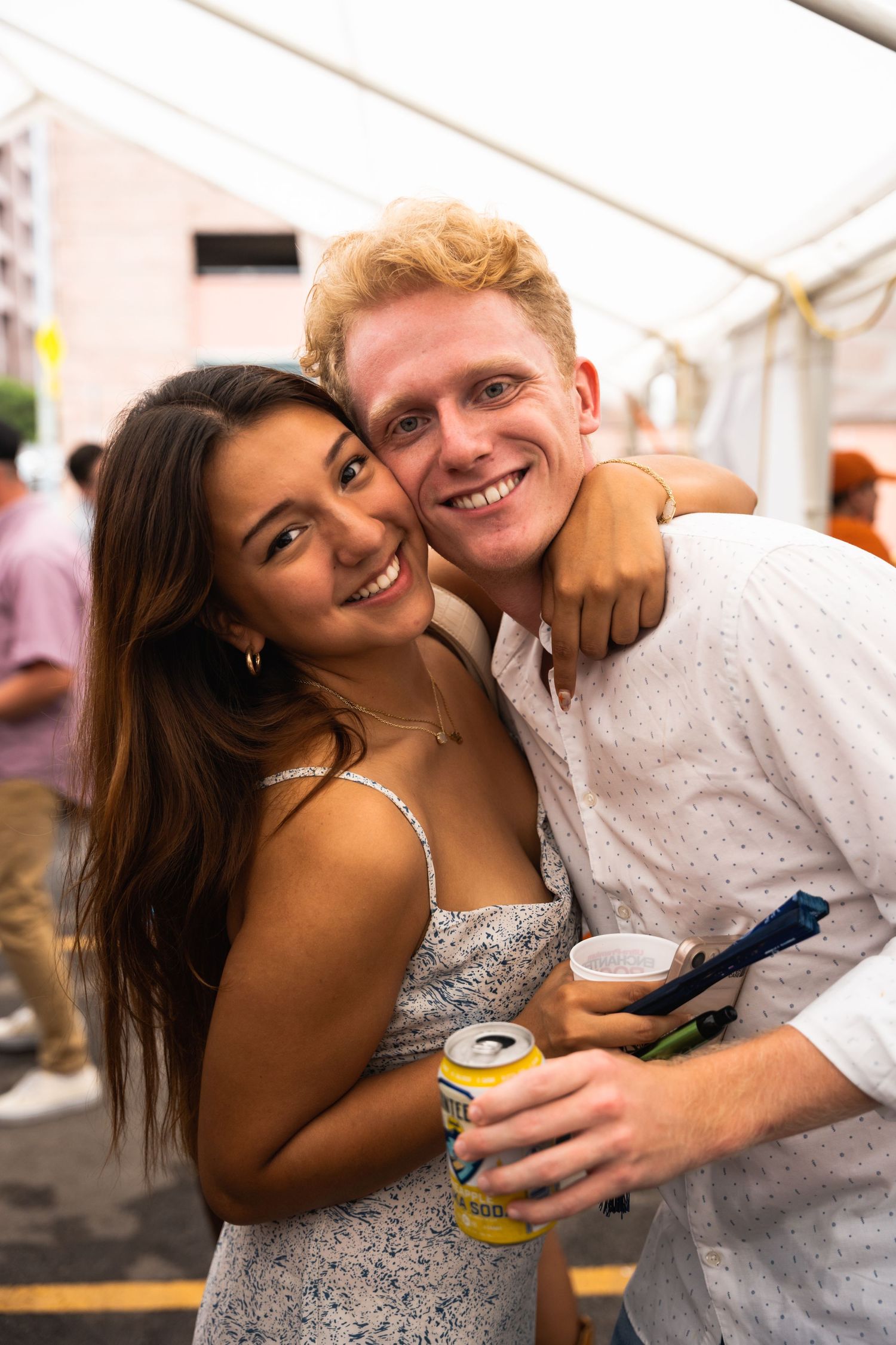 Happy couple embracing and smiling while holding beverages at an outdoor party.