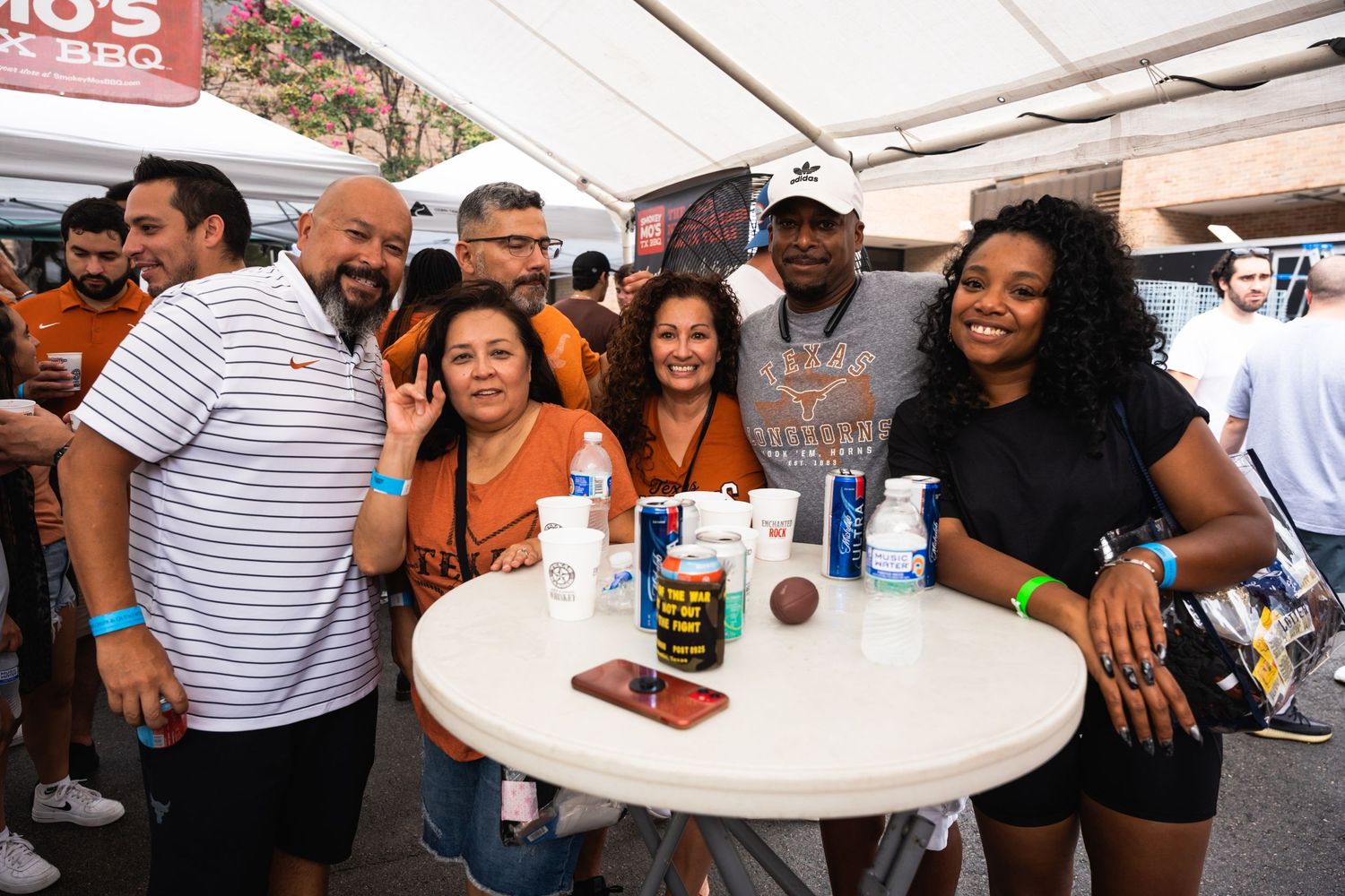 Group of friends gathered around a white table with drinks at an outdoor festival.