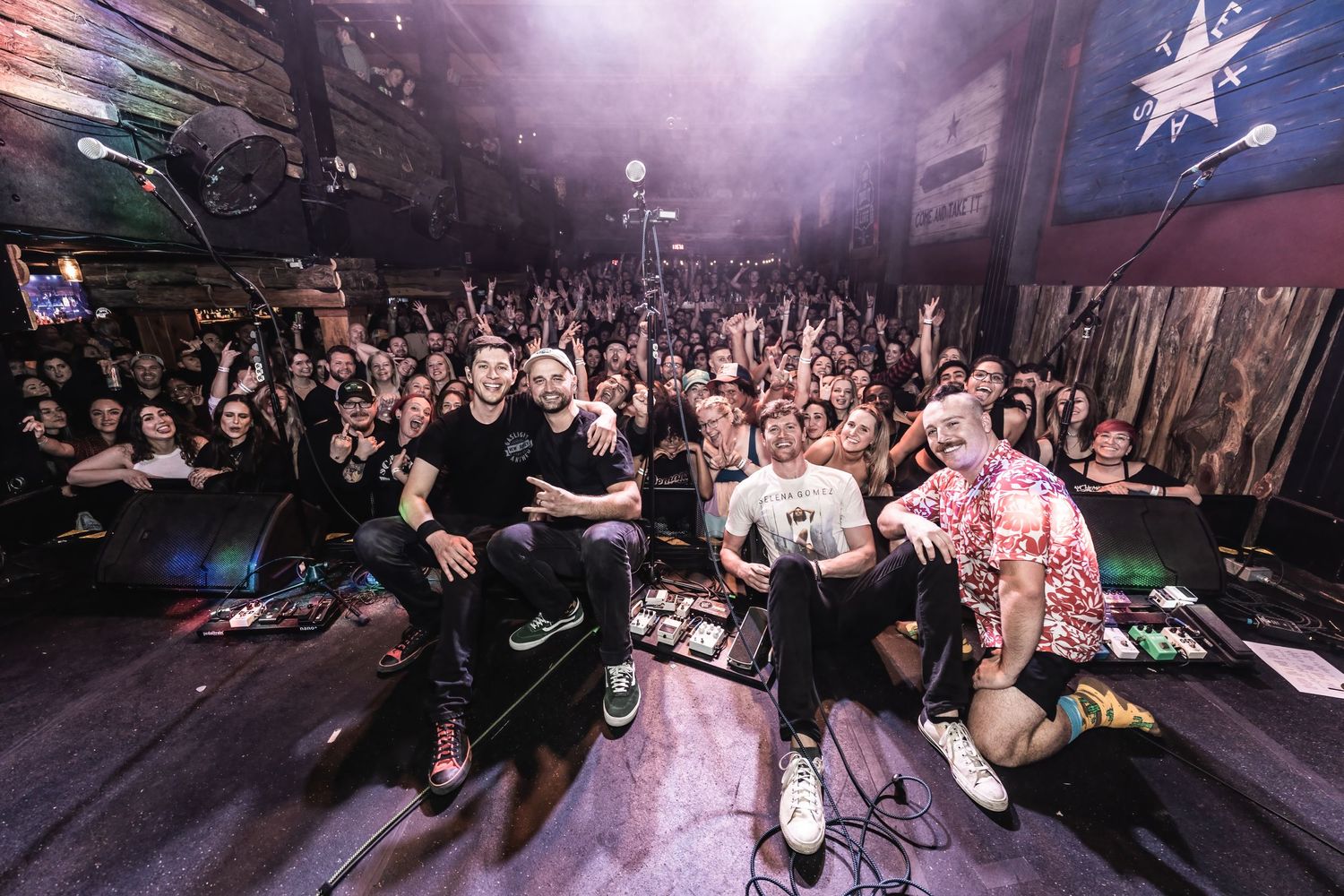 Wide angle shot of concert crowd with raised hands and stage lighting creating atmospheric scene.