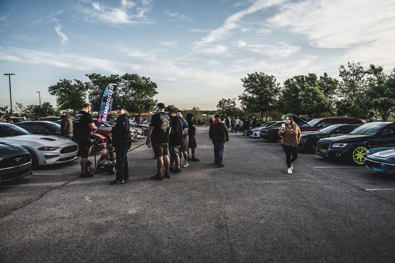 Car enthusiasts gathered in a parking lot at a sunset automotive meetup.