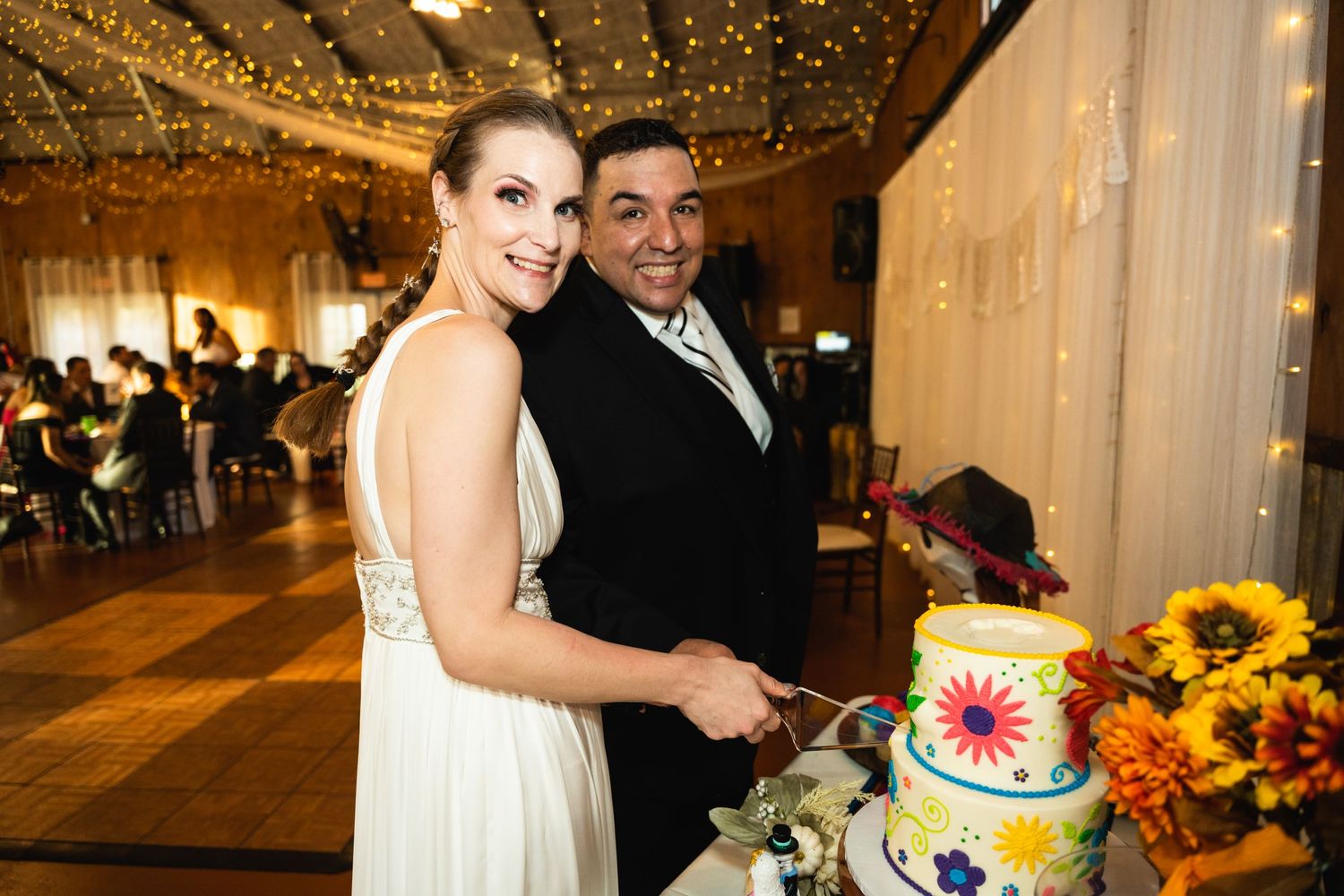 Wedding reception scene with colorful floral cake and string lights creating warm ambiance.