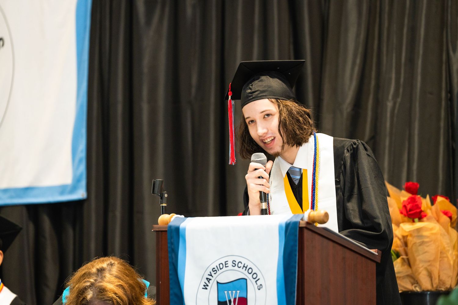 A graduate gives a speech at a podium during a graduation ceremony.