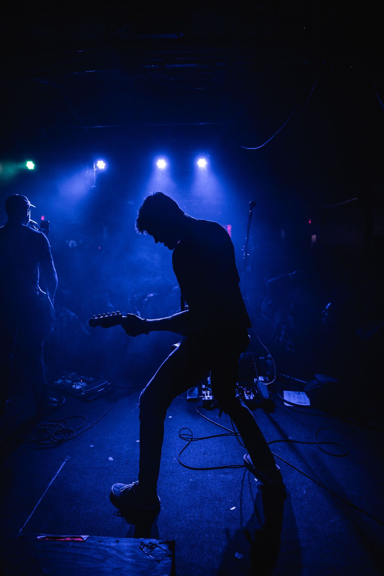 Silhouetted guitarist performs under vibrant blue stage lights during an intense concert moment.