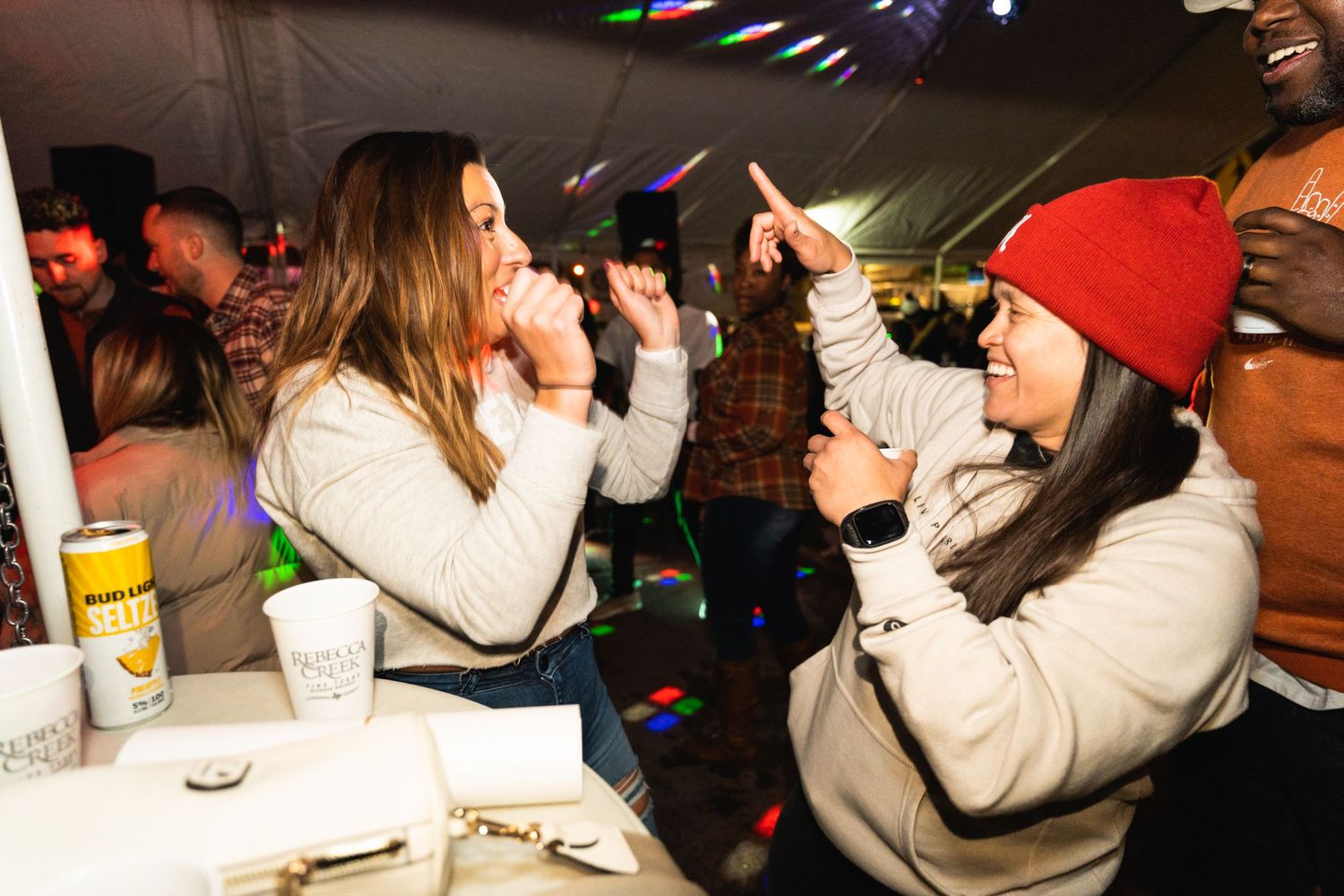 People singing and dancing enthusiastically at a nighttime party with colorful lighting effects.
