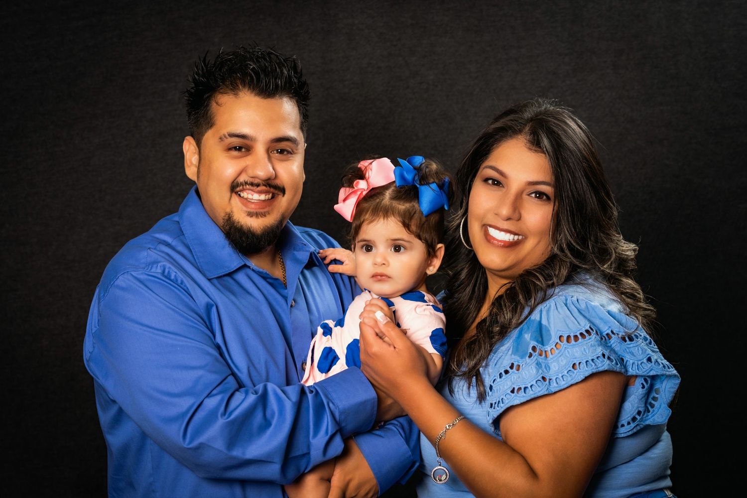 Happy family portrait with parents holding their baby daughter in matching blue outfits.