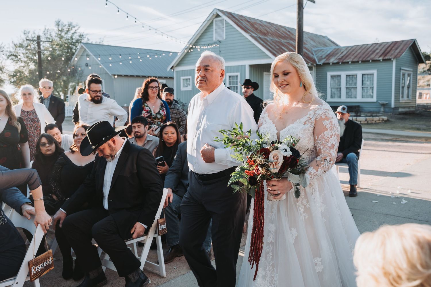 A wedding ceremony processional walking outdoors with a blue house in the background.