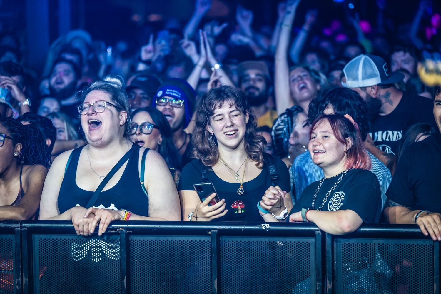 Enthusiastic crowd at concert barrier smiling and cheering during performance.
