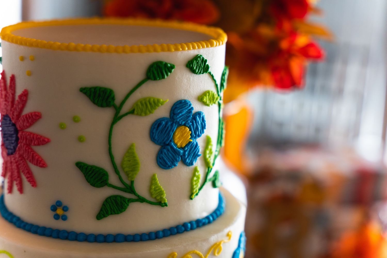 Close-up of a white wedding cake with bright floral decorations and blue trim.