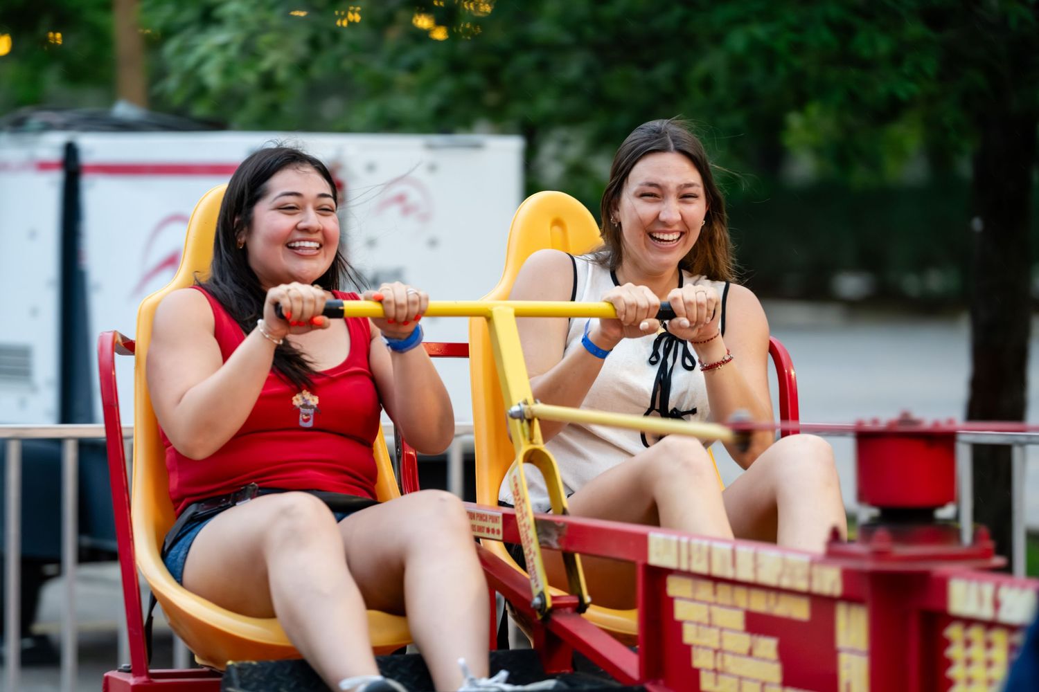 Two young women laughing and enjoying a carnival ride together at an outdoor amusement park.