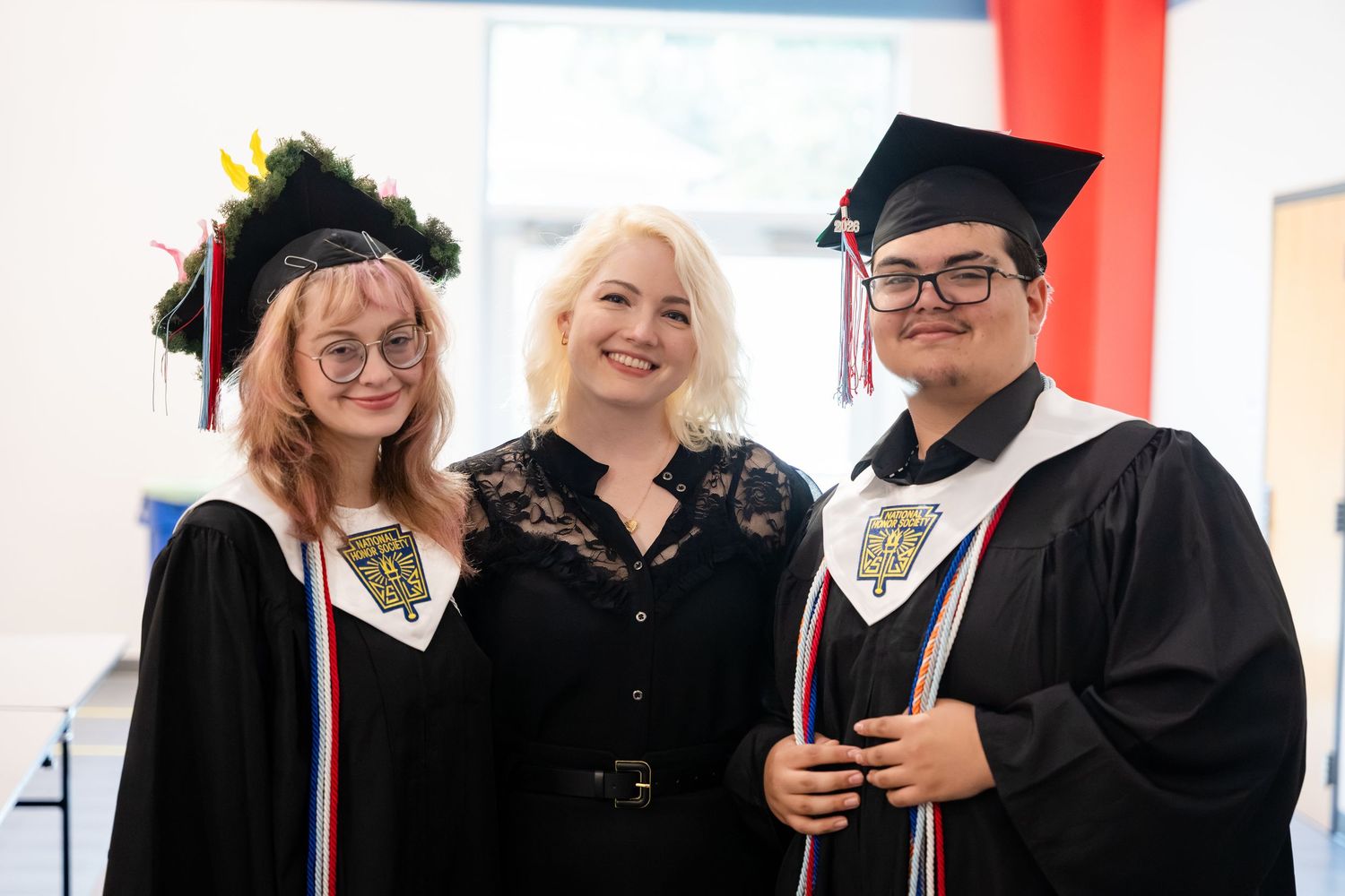 Three smiling graduates in black caps and gowns pose together at a graduation ceremony.