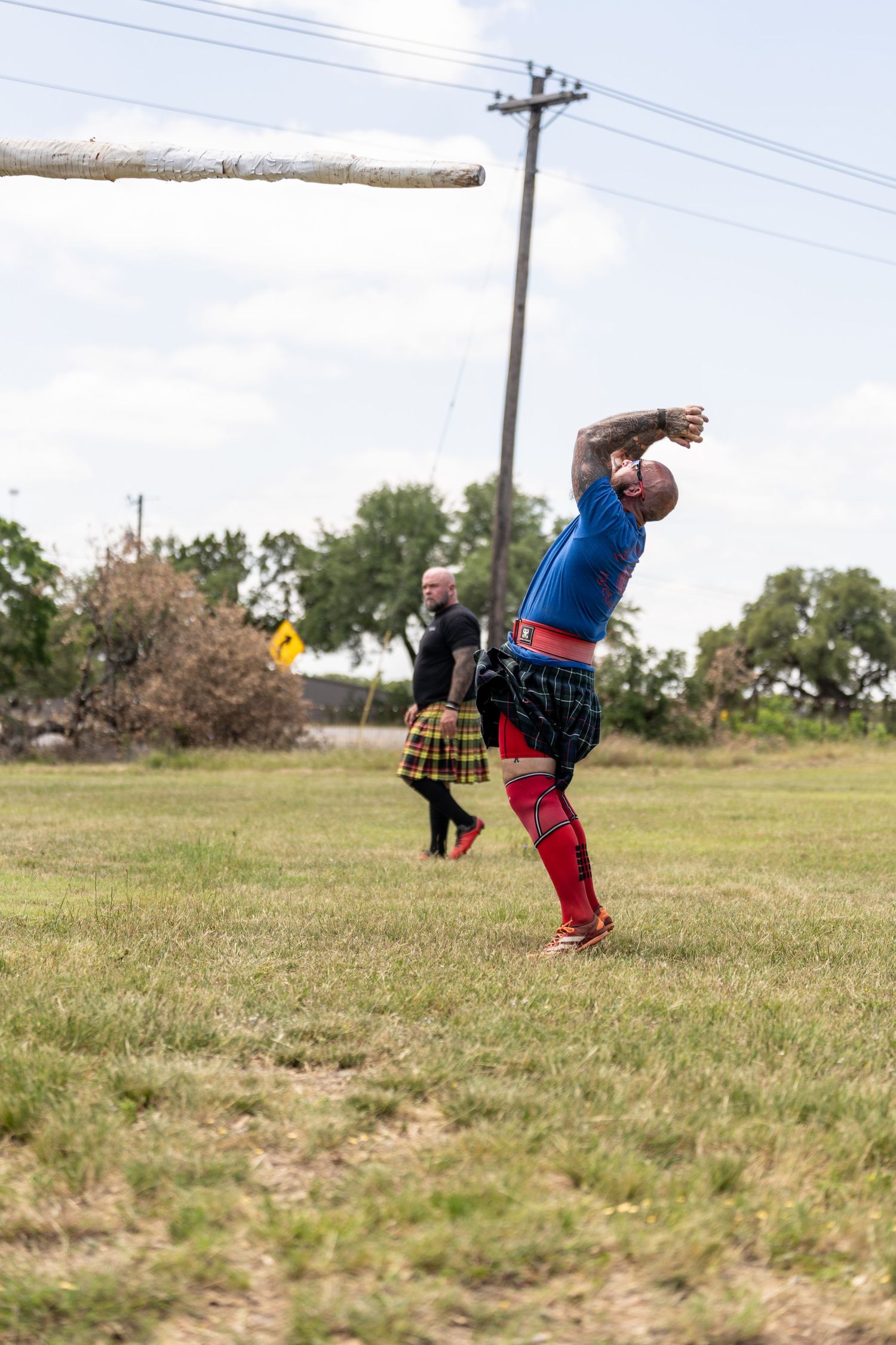Athlete in blue shirt and kilt tosses a caber at a Highland Games competition outdoors.
