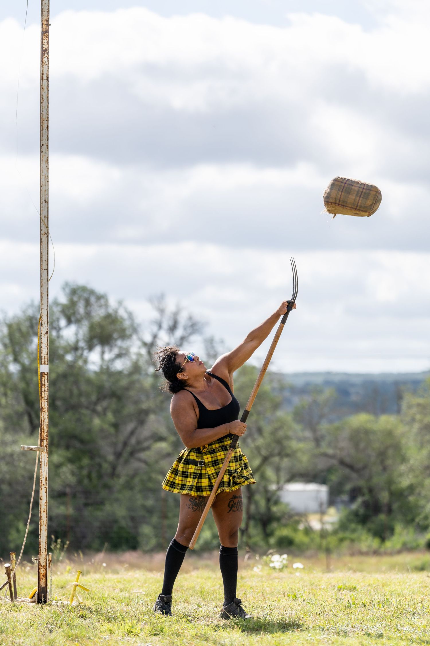 Woman in plaid skirt and knee socks tossing a wicker basket with a blade outdoors.