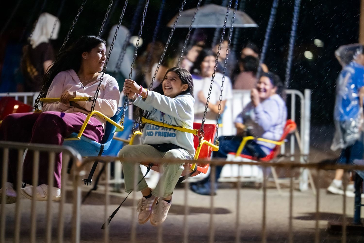 People enjoying a swing carousel ride at a nighttime fairground, smiling and having fun under bright lights.