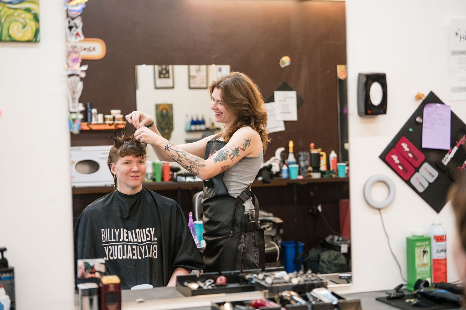 Stylists work at various stations in a modern hair salon with black chairs and mirrored workstations.