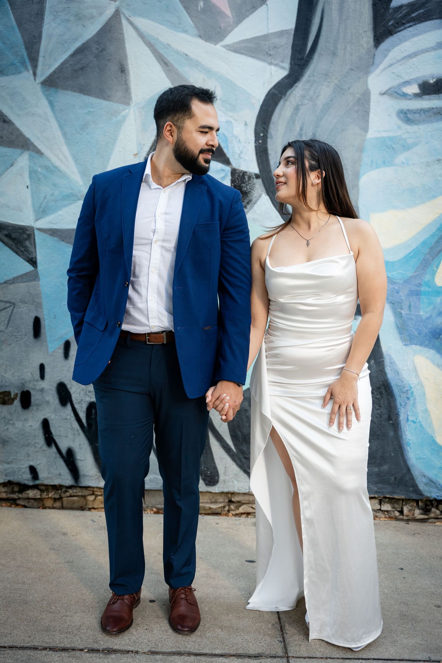 A couple in wedding attire poses against a geometric blue wall mural in an artistic photo series.