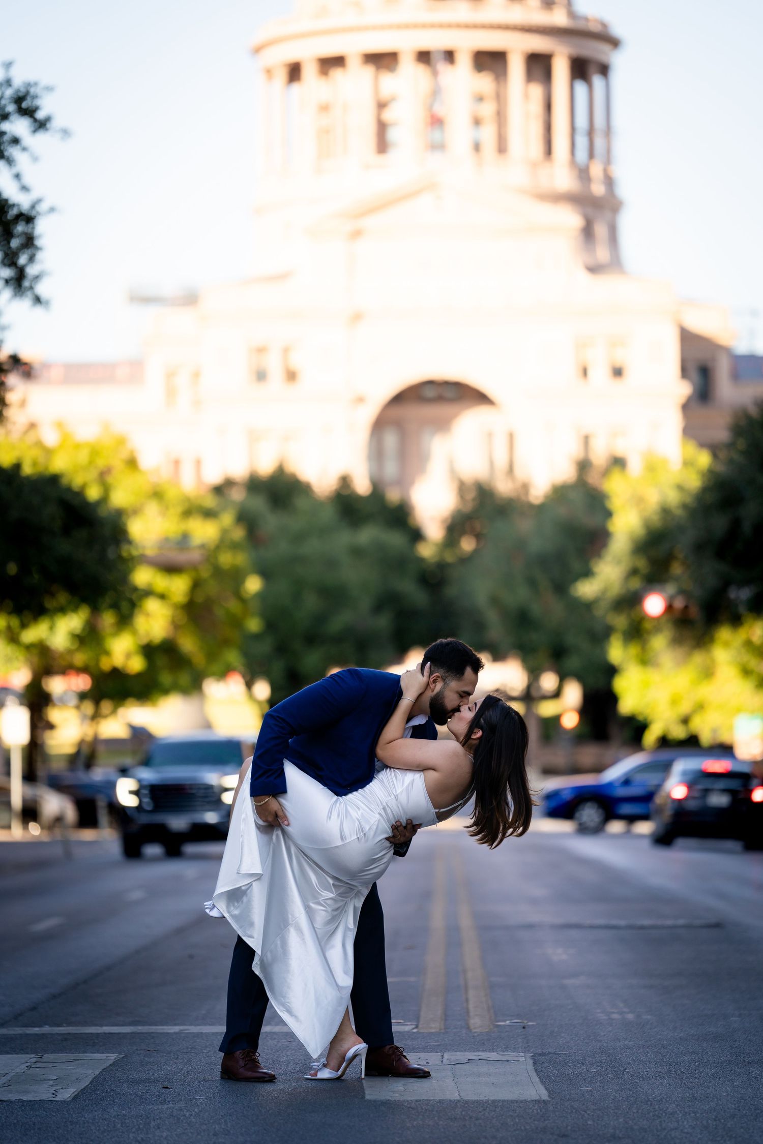 A romantic couple performs a dip pose in front of the Texas State Capitol building at sunset.