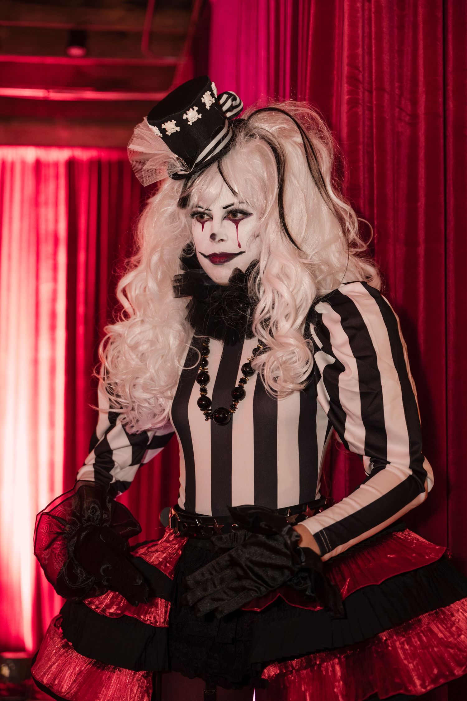 A performer in a black and white striped dress with red tulle skirt poses dramatically against red curtains.