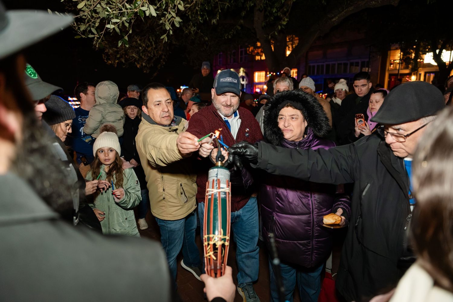 Crowd of people gathered outdoors at night holding up a large bottle in celebration.