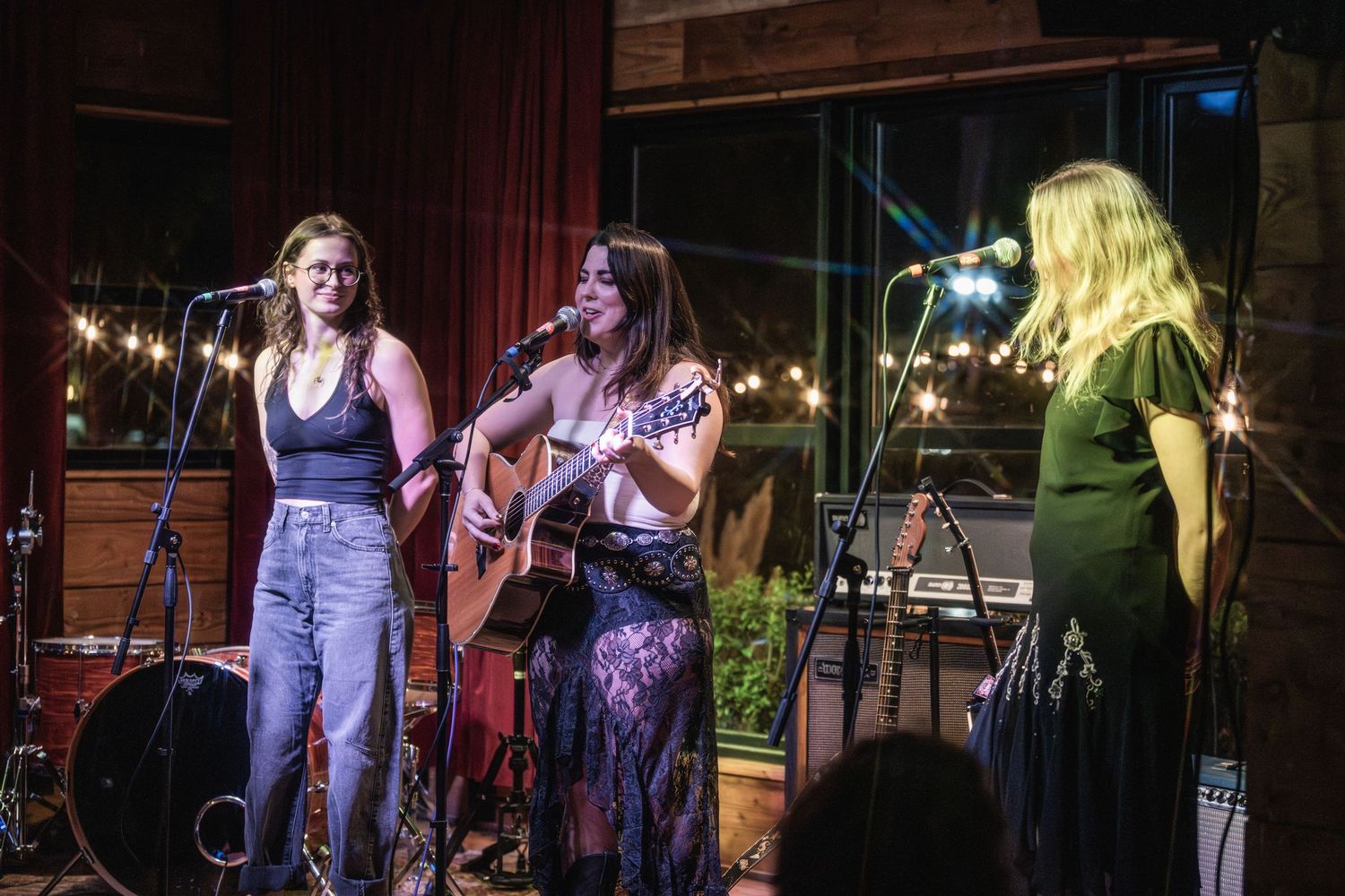 Musicians perform on stage at a live music venue with string instruments and microphones under warm lighting.