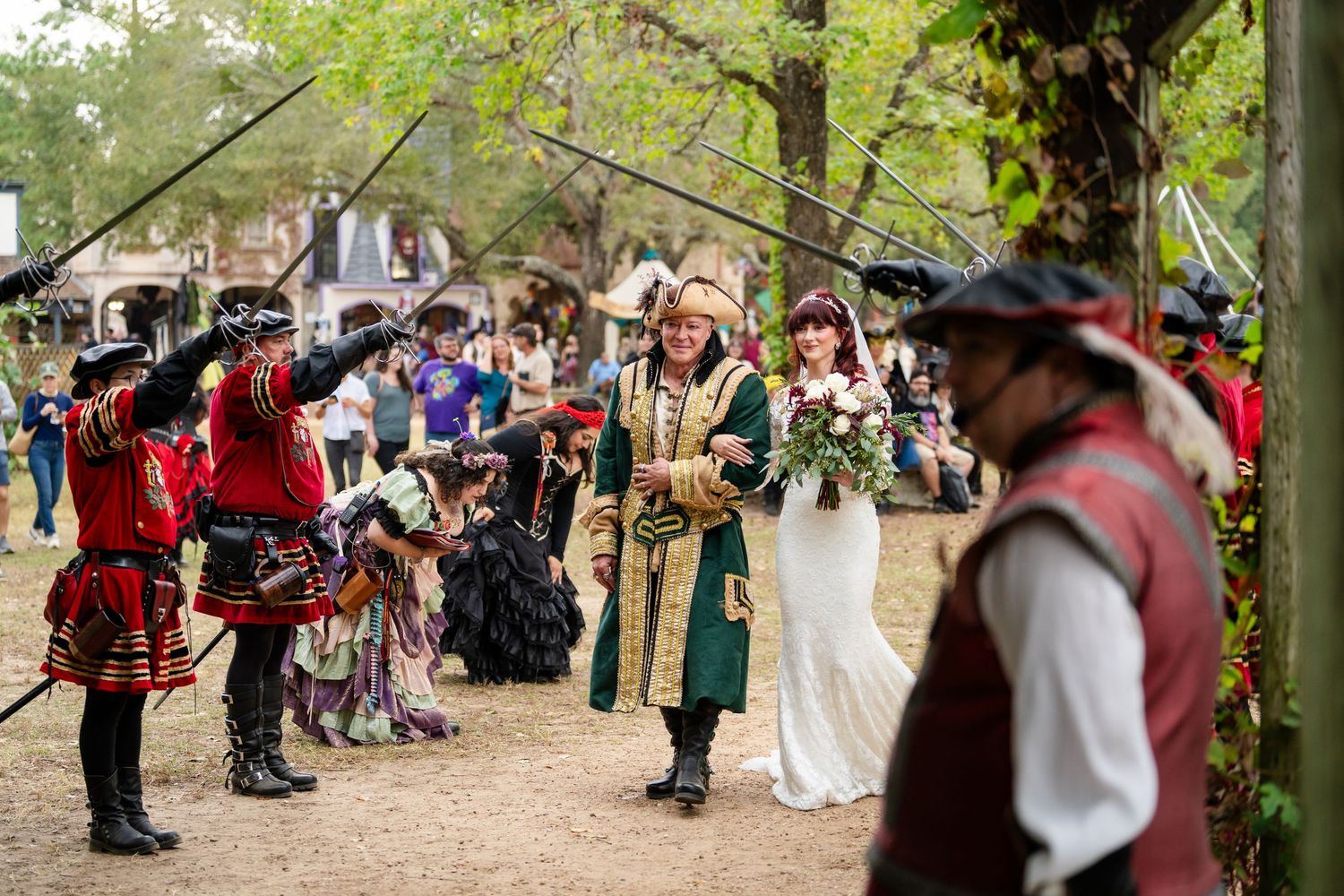 People in medieval and renaissance costumes dance in a circle at an outdoor festival.