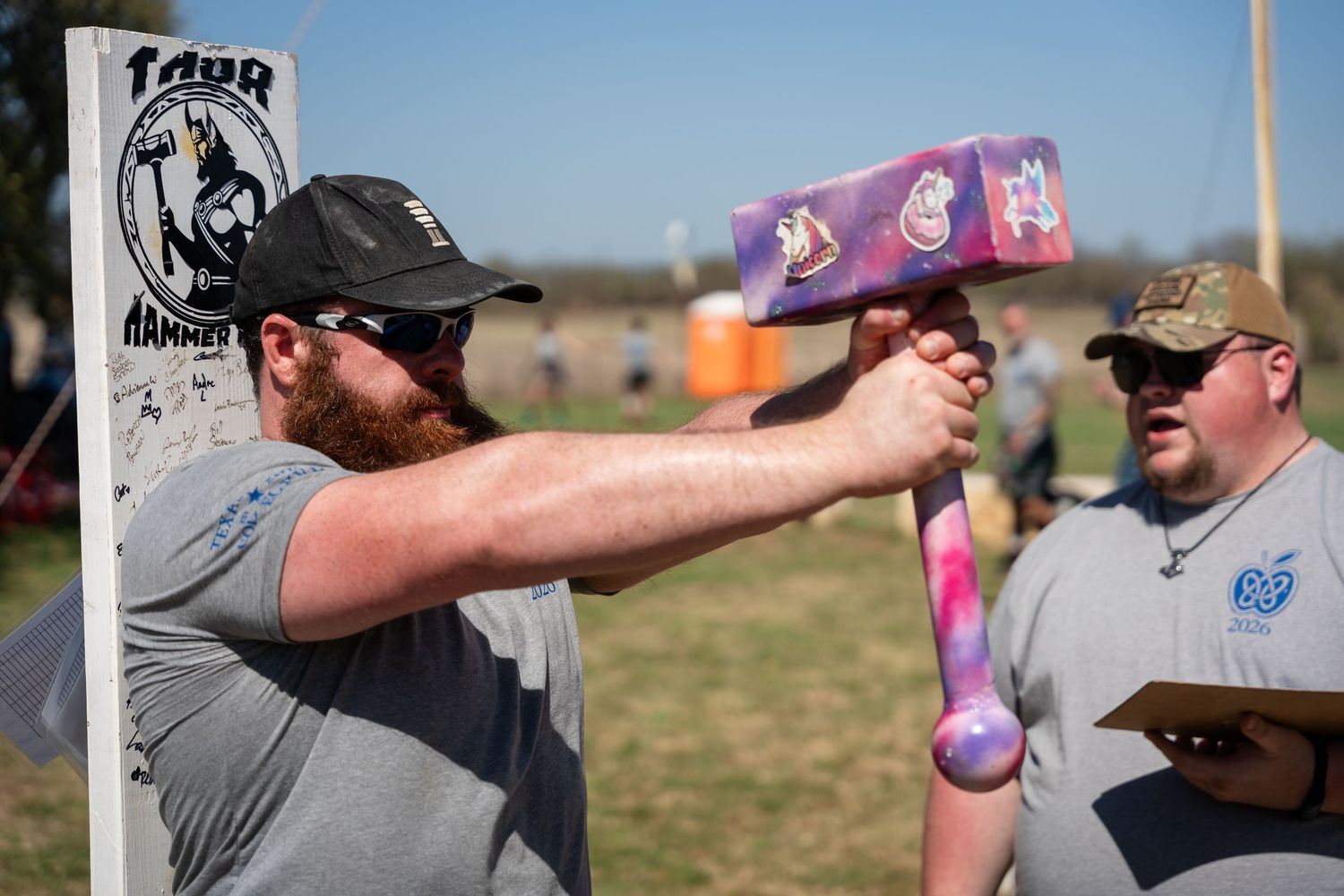 Man swinging a colorful oversized foam hammer at an outdoor event with spectators in the background.