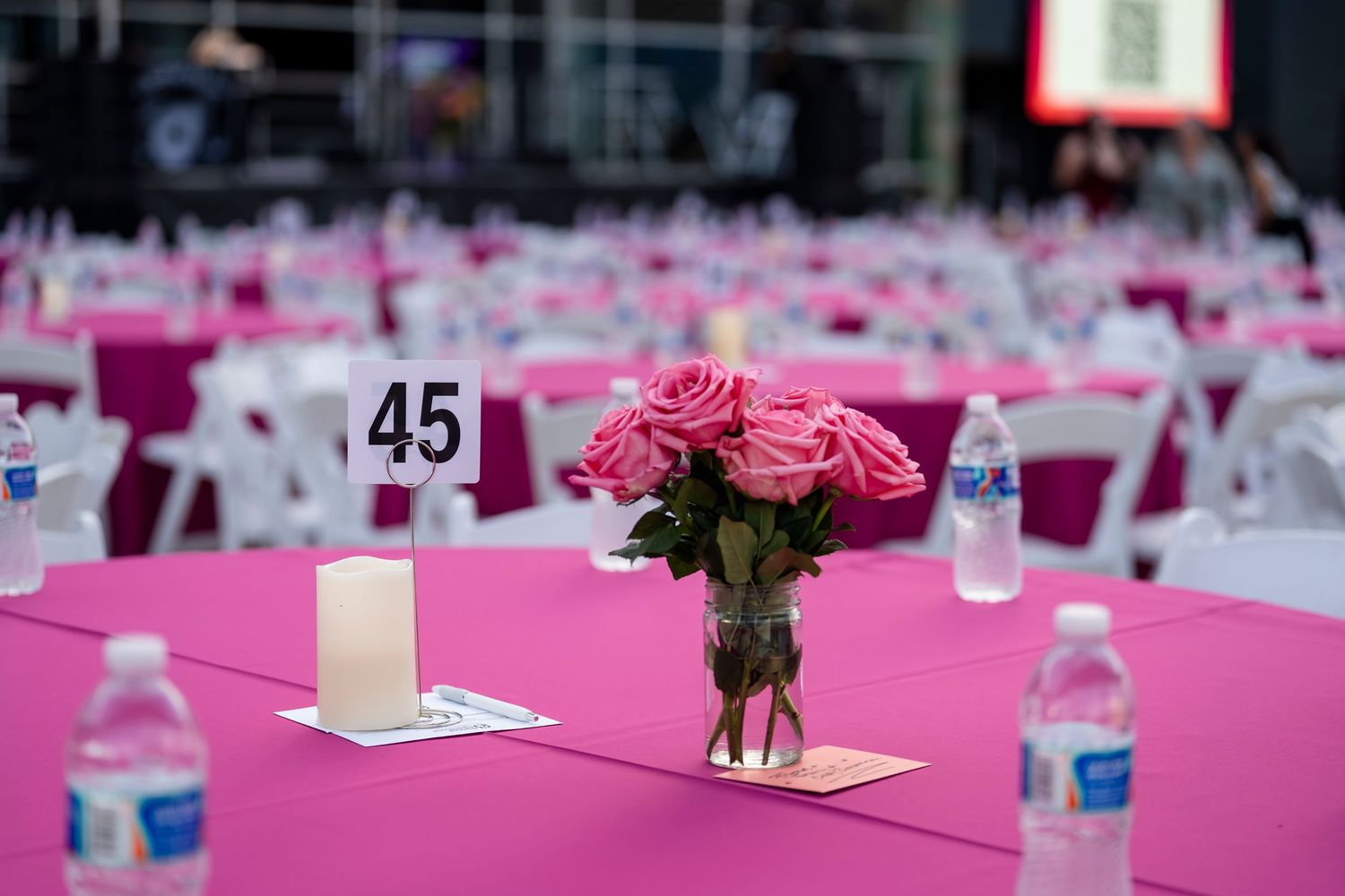 Long banquet tables with pink tablecloths and white place settings stretch across an elegant event space.