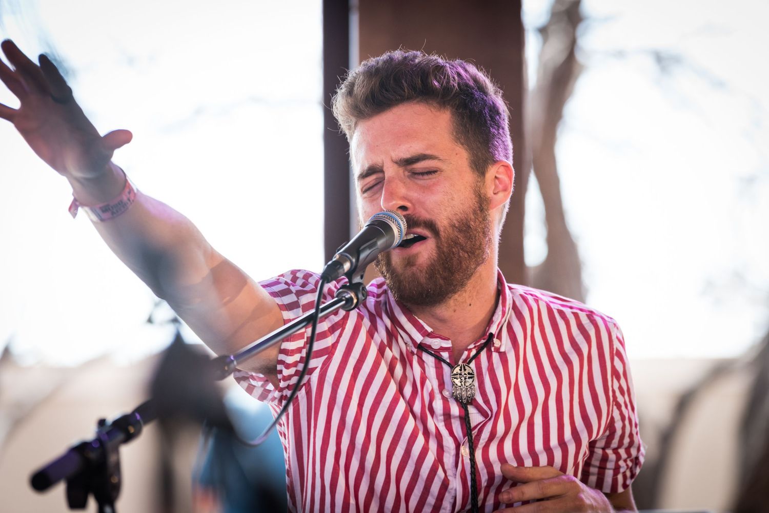 A singer performs passionately on stage wearing a red and white striped button-down shirt.
