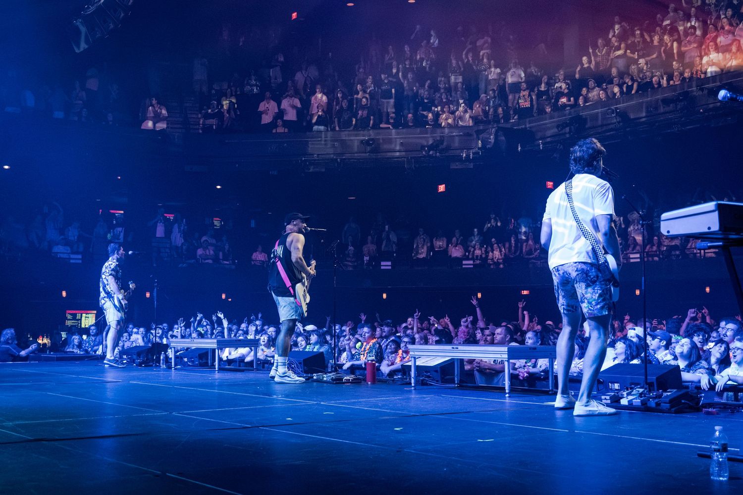 Performers on stage at a packed concert venue with blue lighting and an engaged crowd in the background.