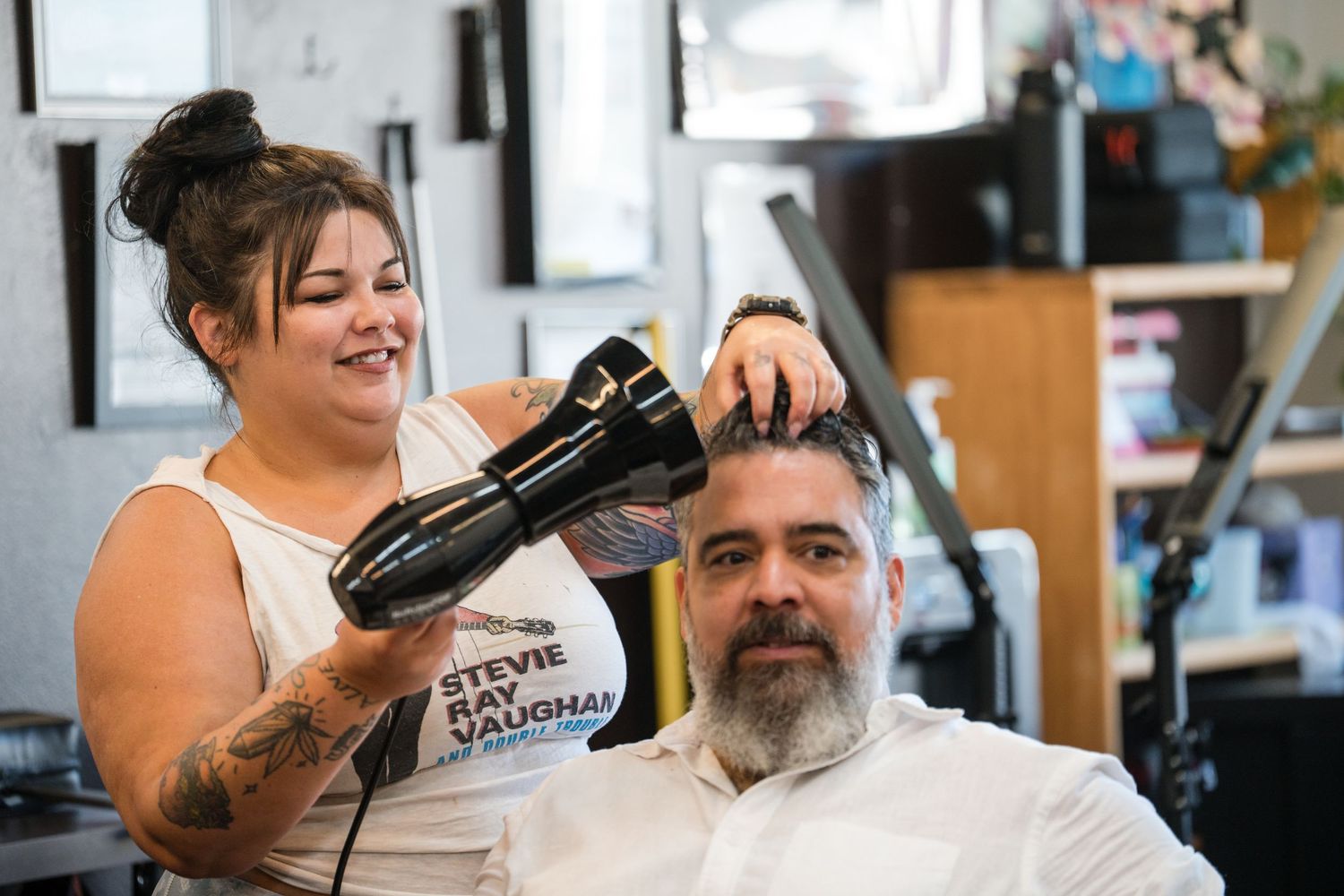 A hairstylist uses a blow dryer while styling hair in a salon setting.