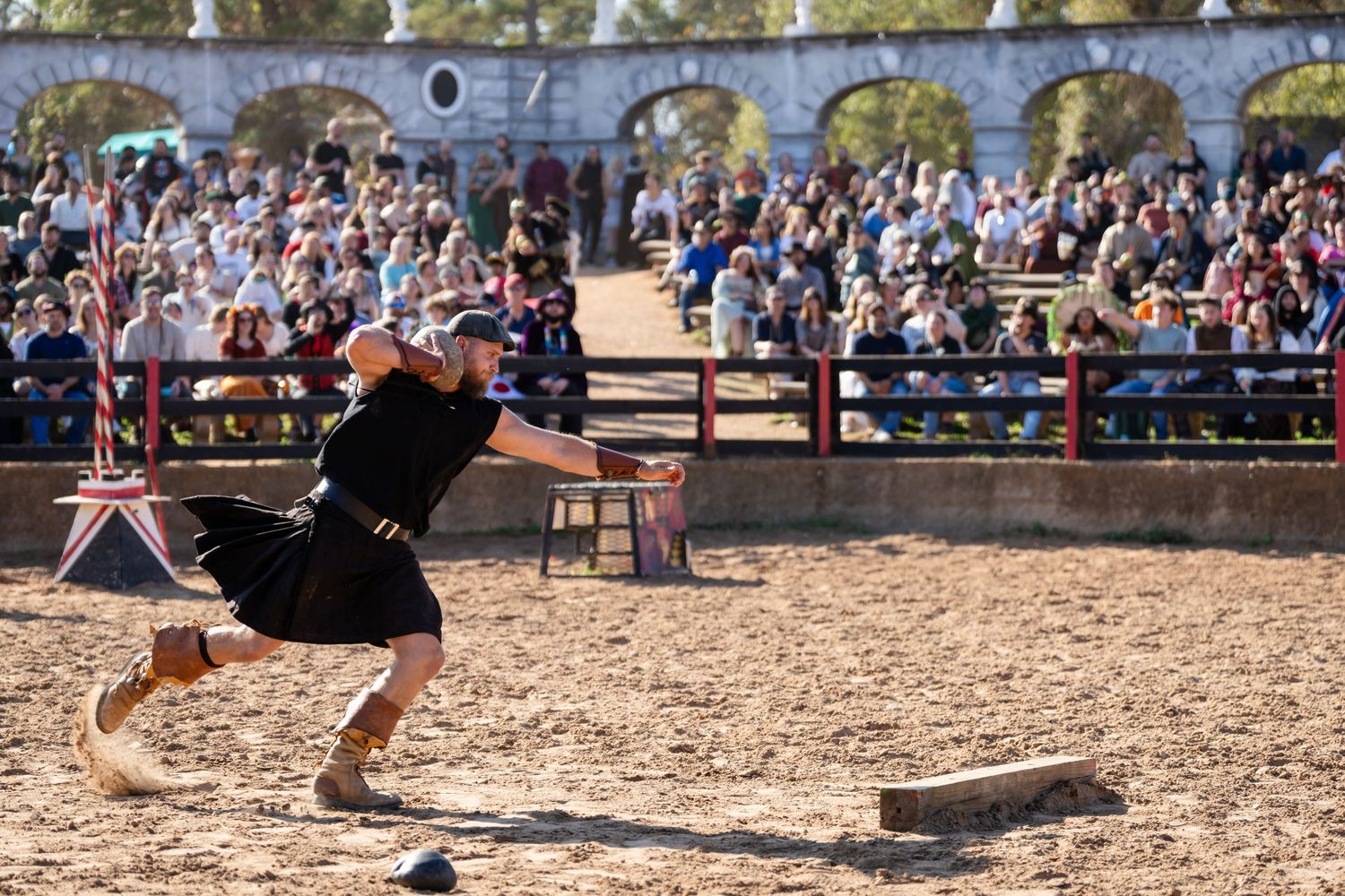 A performer in medieval costume demonstrates sword fighting techniques at a renaissance fair in front of a large crowd.