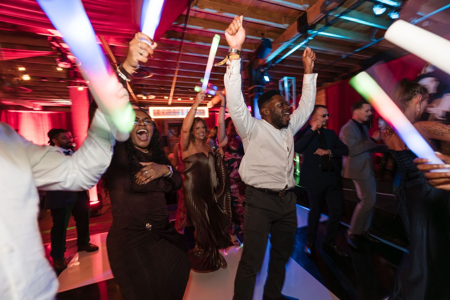Crowd of people dancing and celebrating at a nightclub with vibrant red lighting and glowing decorations.