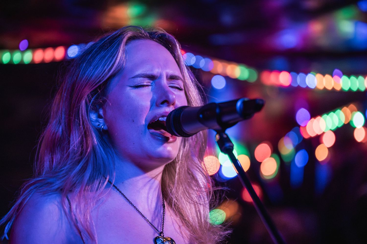 Singer performs passionately on stage with colorful bokeh lights creating a dreamy atmosphere in the background.