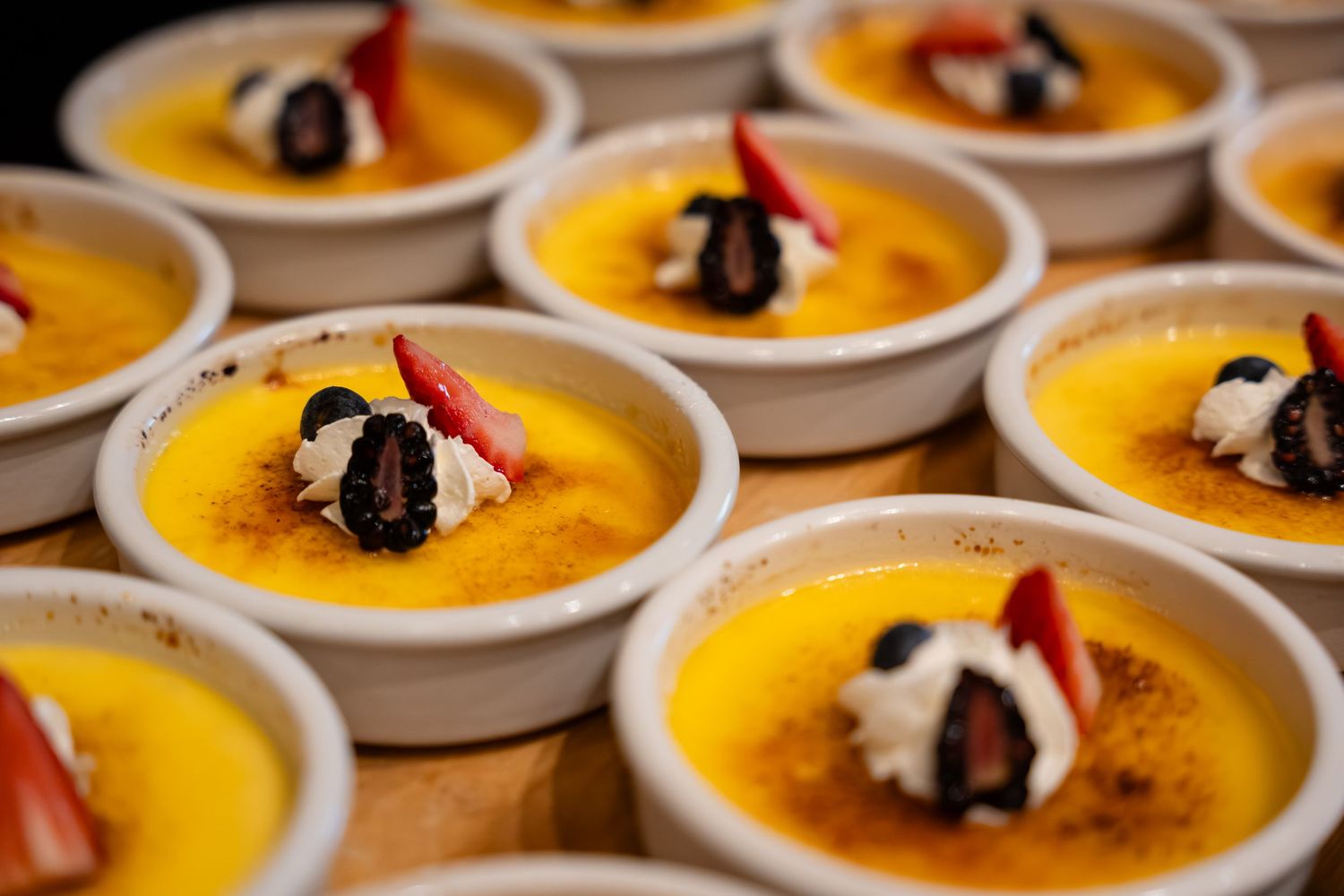 Elegant creme brulee desserts in ramekins topped with whipped cream, fresh strawberries, and chocolate garnish.
