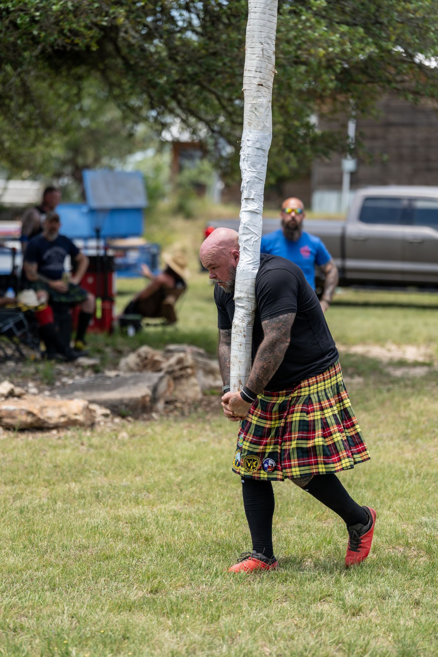 Man in tartan kilt tossing caber at Highland Games competition outdoors.