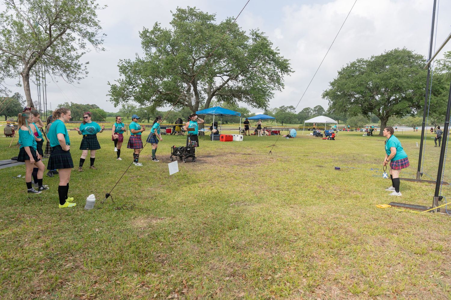 Girls in teal uniforms practice on a grassy field during an outdoor sports tournament with tents in background.