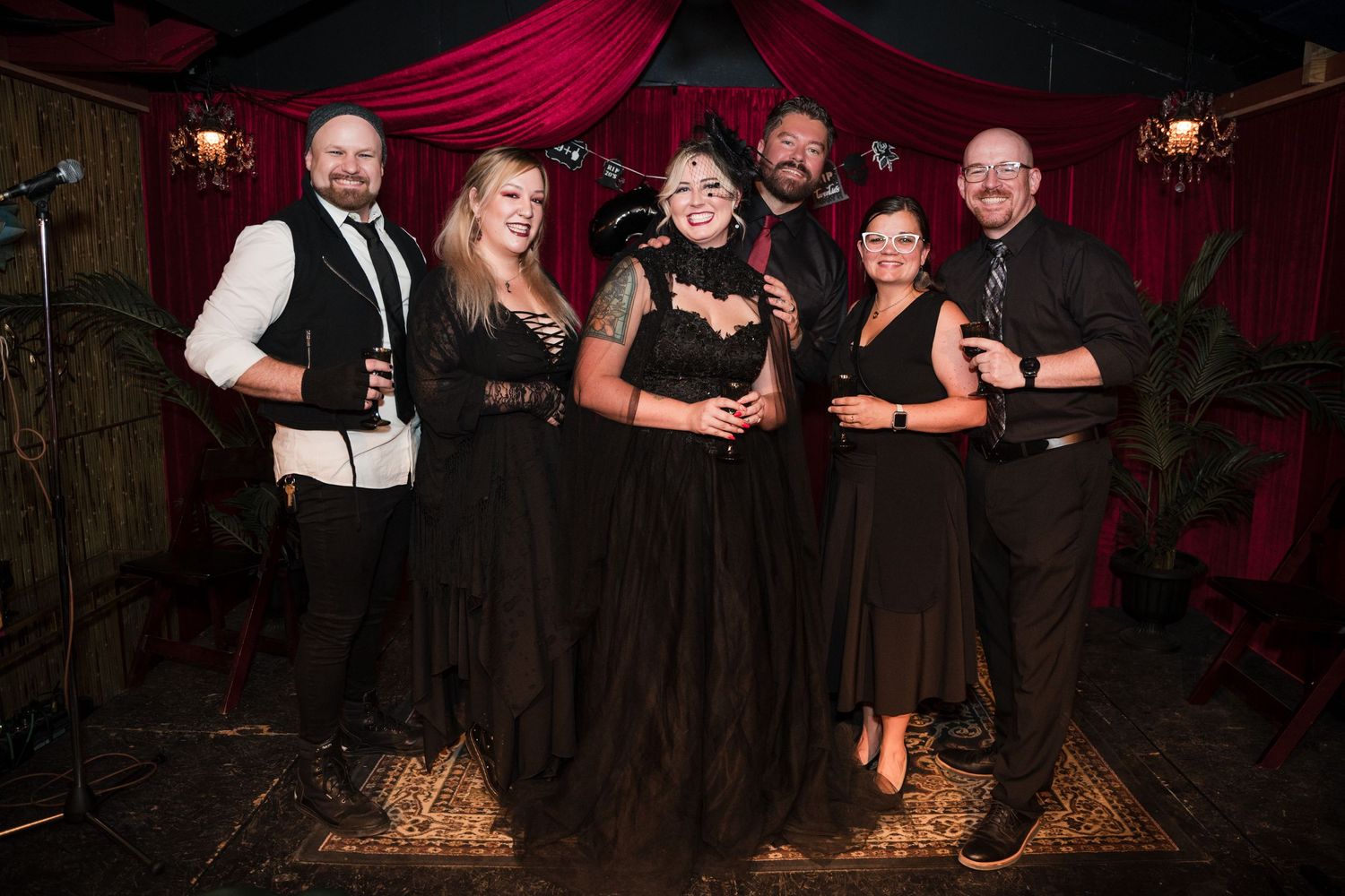 A group in formal black attire poses against a dark red velvet backdrop at an event.