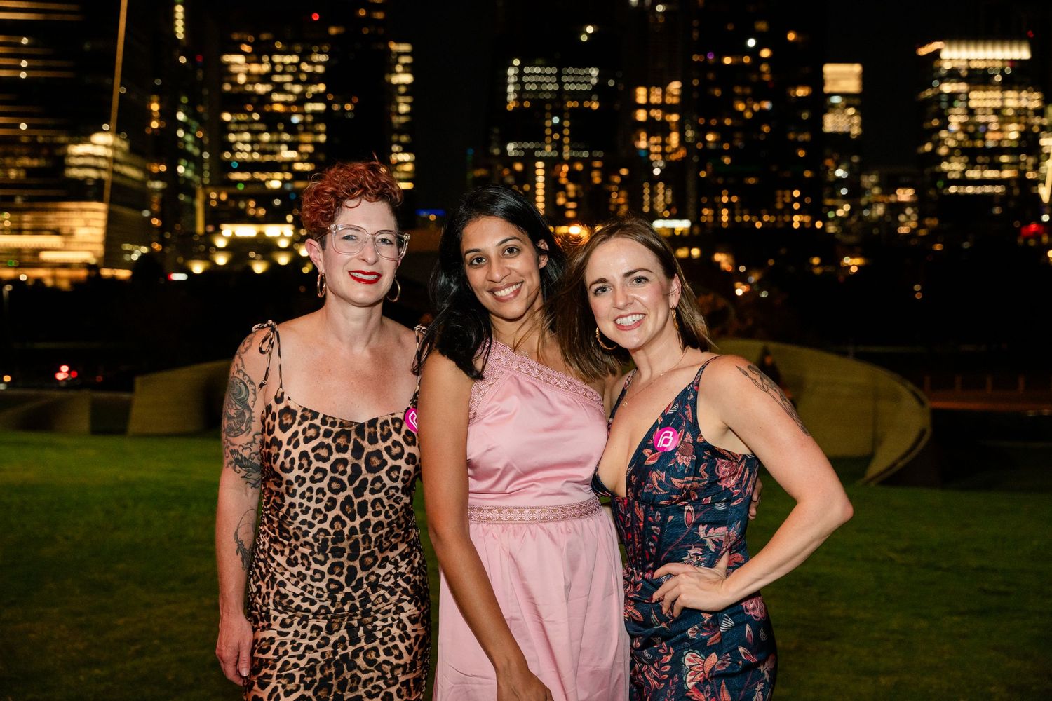 Friends pose together at night event with urban skyline background.